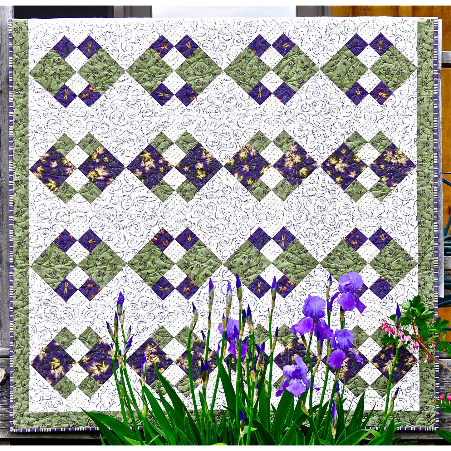 Geometric quilt pattern in shades of greens and purples on a white background.