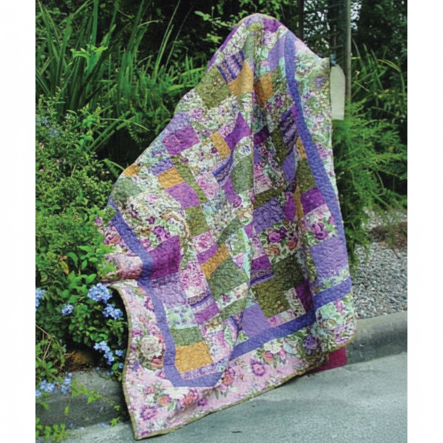 Pretty floral quilt shown draped in a garden.