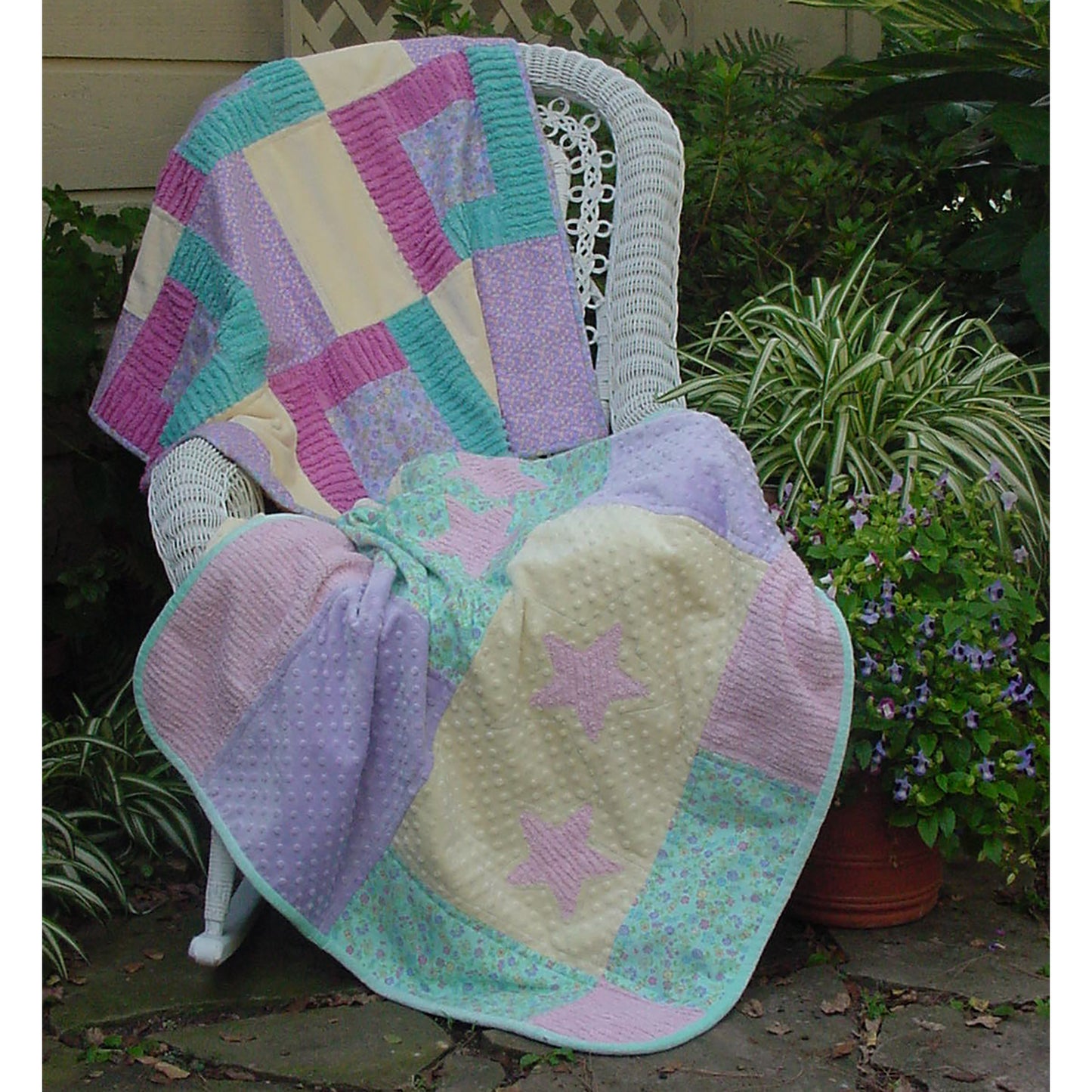 Two baby quilts draped over a chair. Top quilt features squares of bright colors. Bottom quilt features pastel blocks with pink stars.