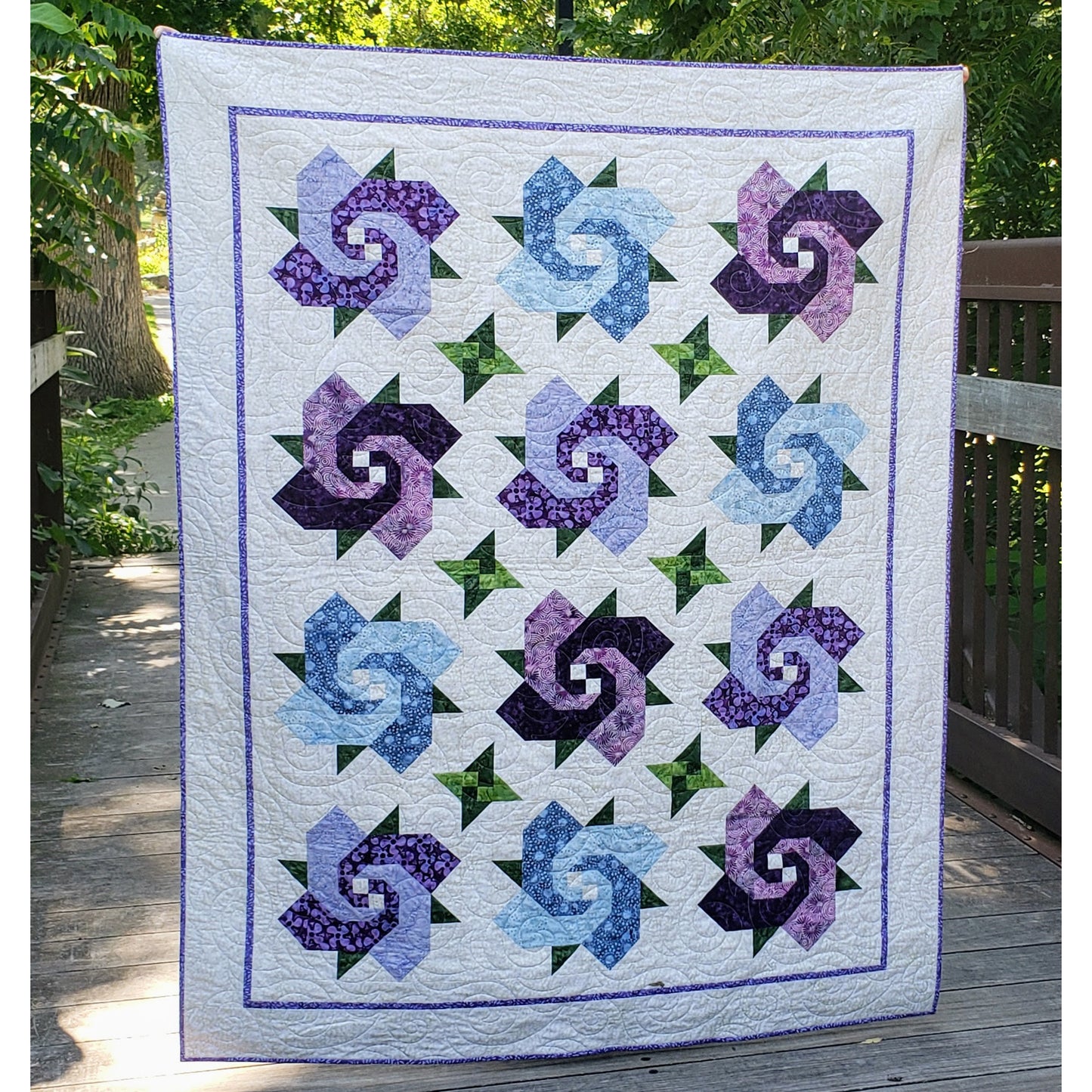 Beautiful floral quilt features large flowers which are made similarly to a snail's trail block. Smaller "leaves" are using card trick.