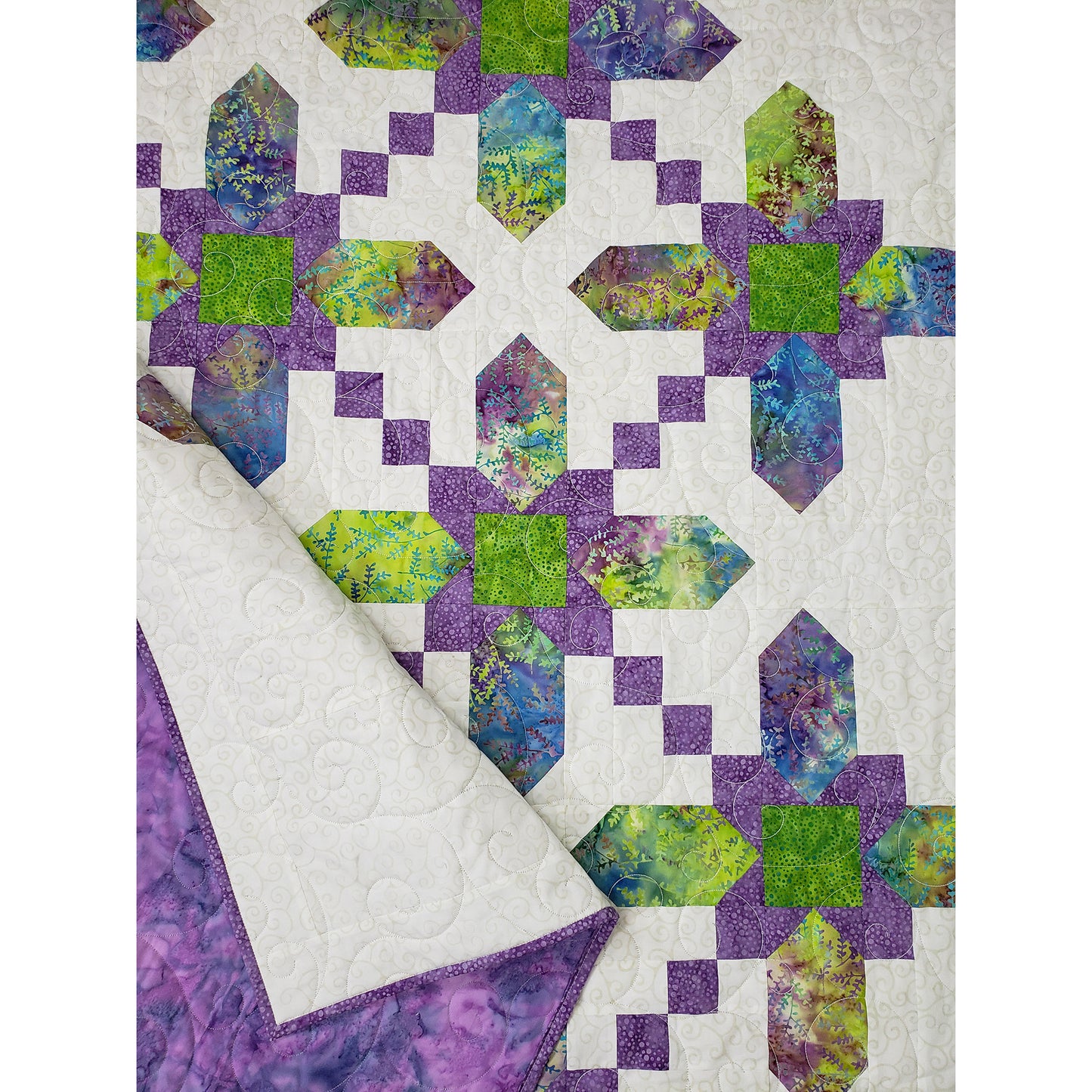 A closeup of a quilt in white, adorned with a prominent flower design in pastel colors. You can see the details of the flowers in this image.