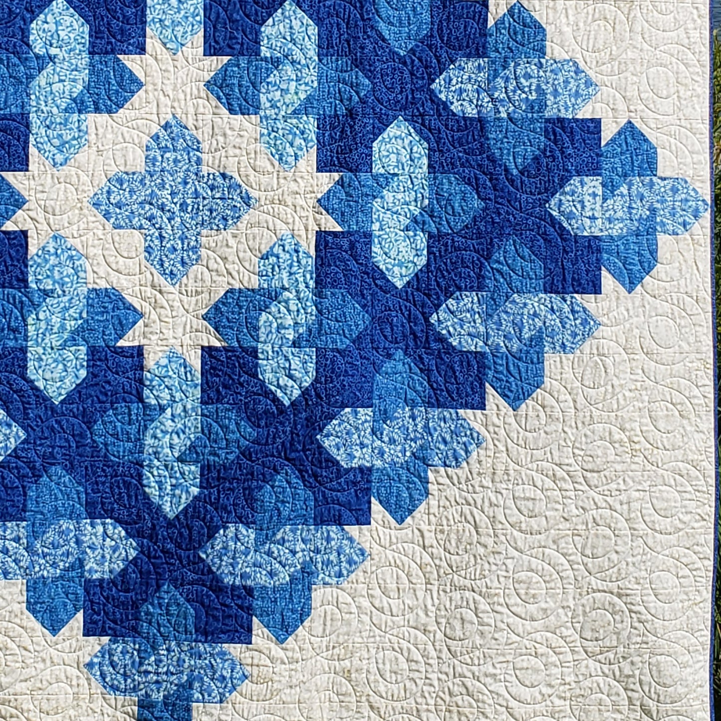 Close up of blue and white quilt featuring an intricate diamond pattern. Can see the smaller elements of Xs interwoven with other elements.