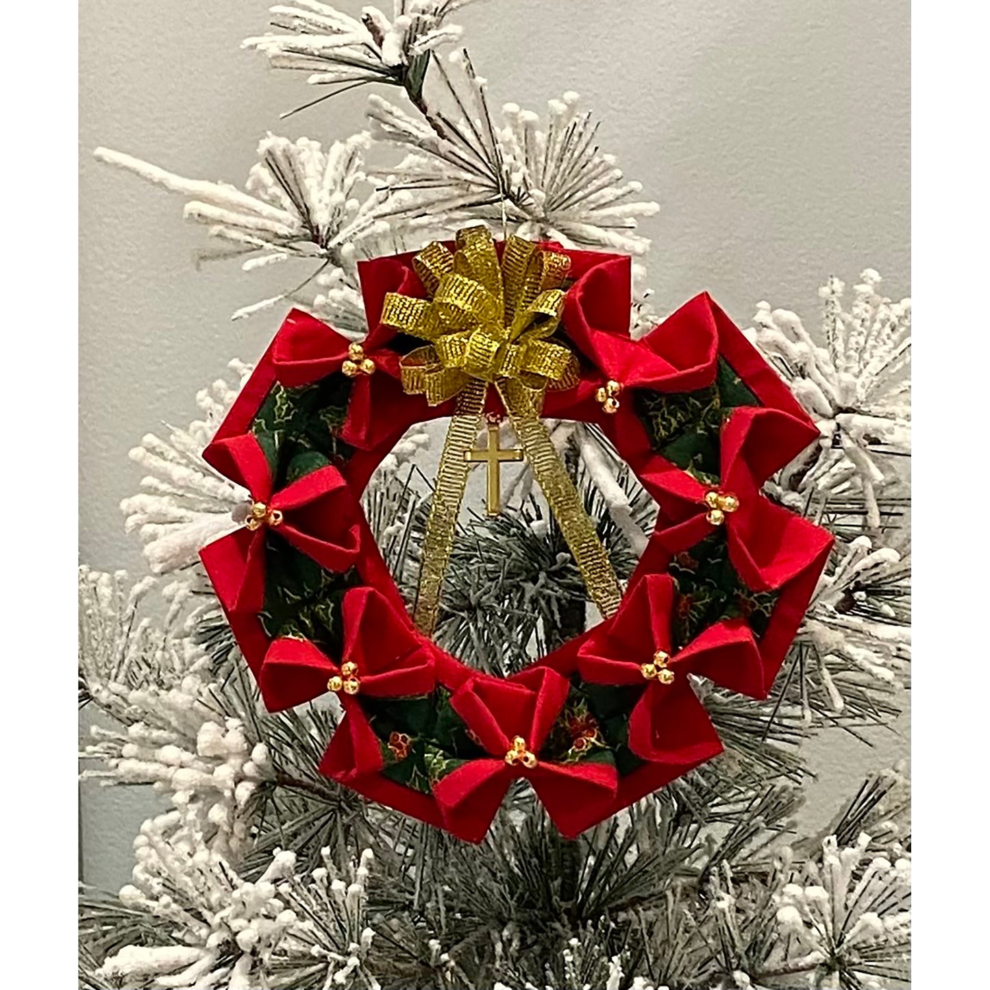 Beautiful wreath ornament with a gold bow on top shown in a white Christmas tree. Unique the way it is pinched around and showcases three gold beads at each of these points.