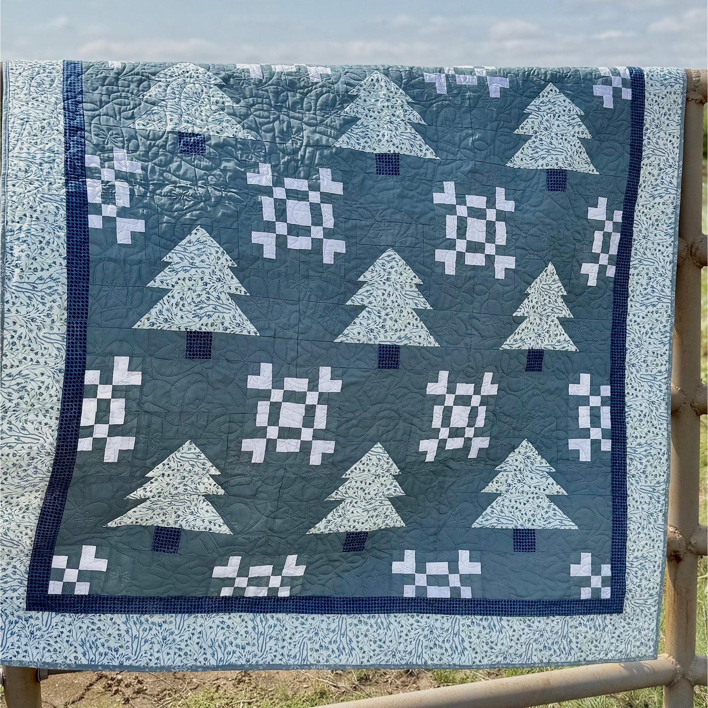 Beautiful winter-themed quilt featuring pine trees and snowflakes. Quilt in blues, making it feel more winter-like.