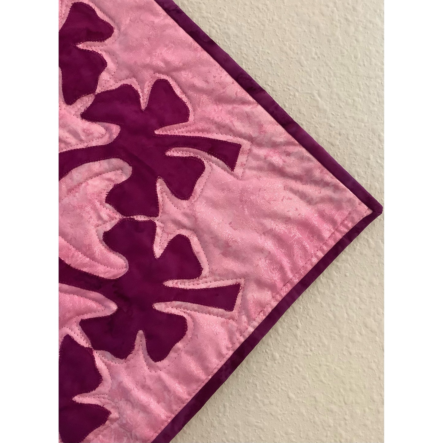 Close up image of one side of design of applique on pink background.