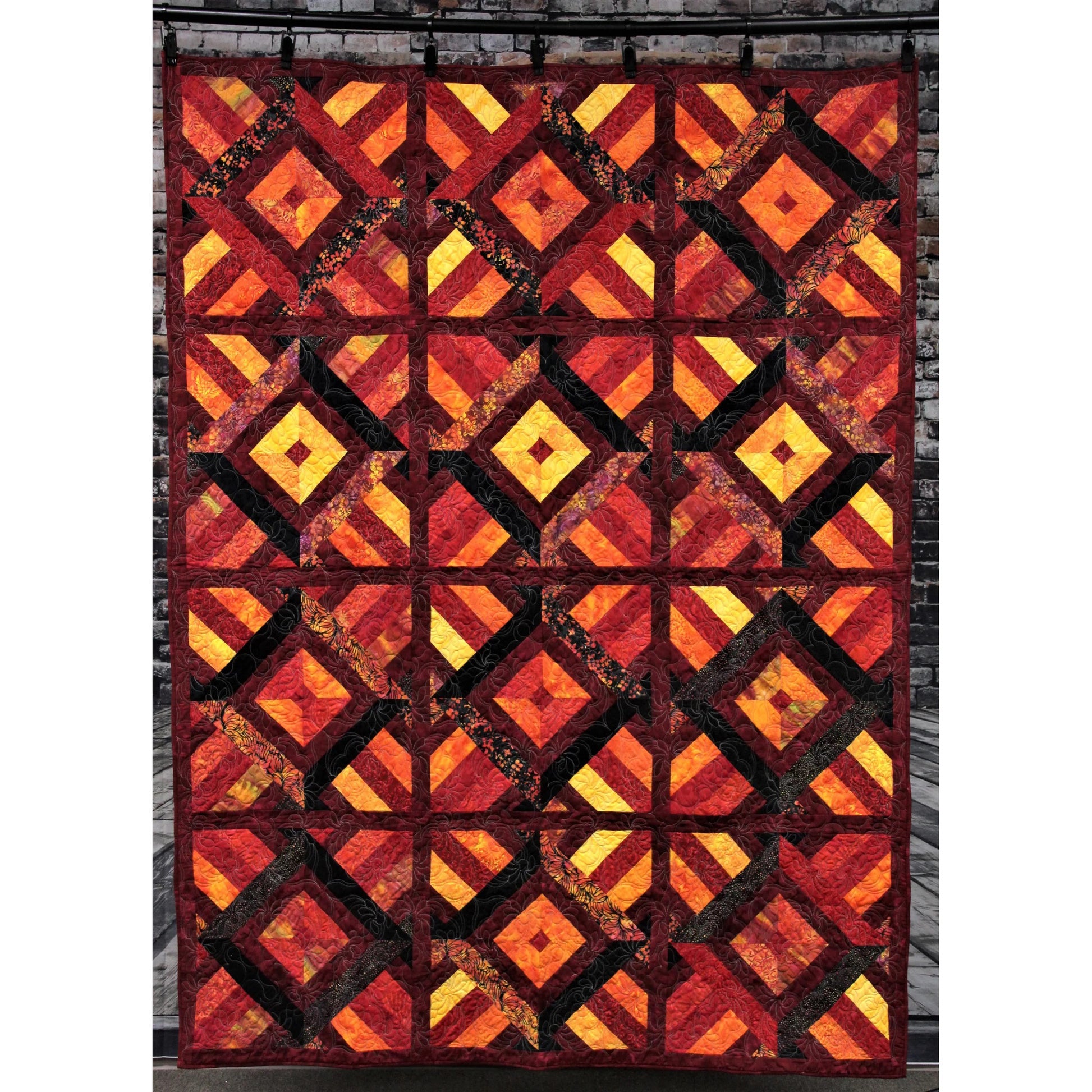 Quilt with a geometric pattern in red, orange, and yellow on a brick wall background