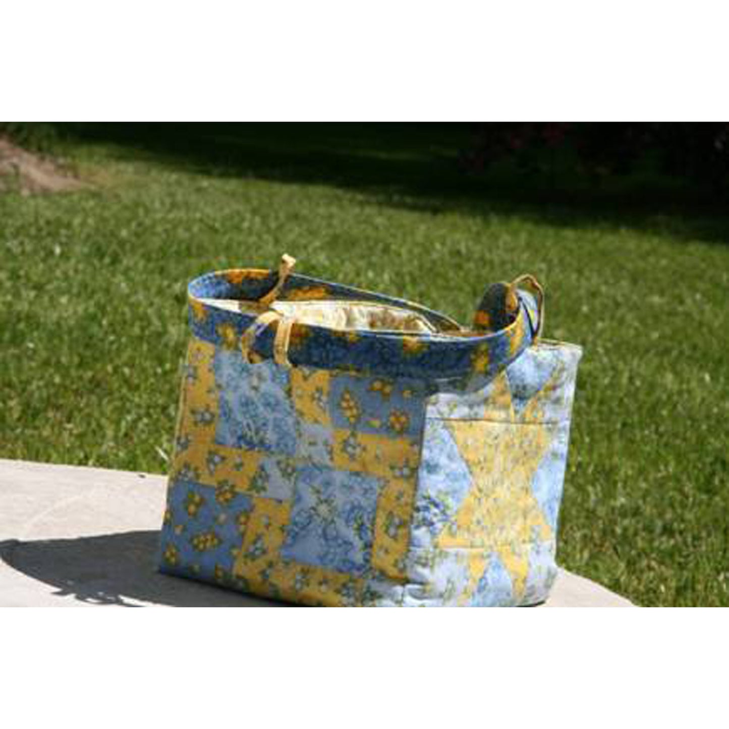 Blue and yellow patterned bag on a white surface with grass in the background