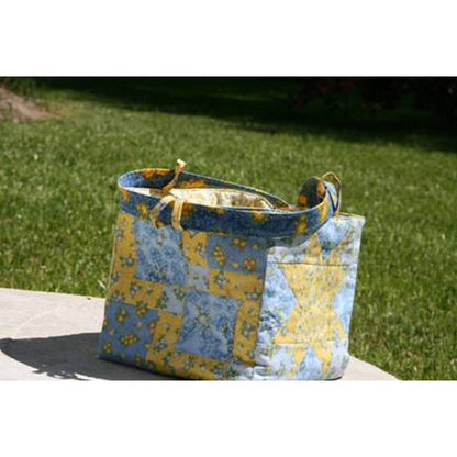 Blue and yellow patterned bag on a white surface with grass in the background