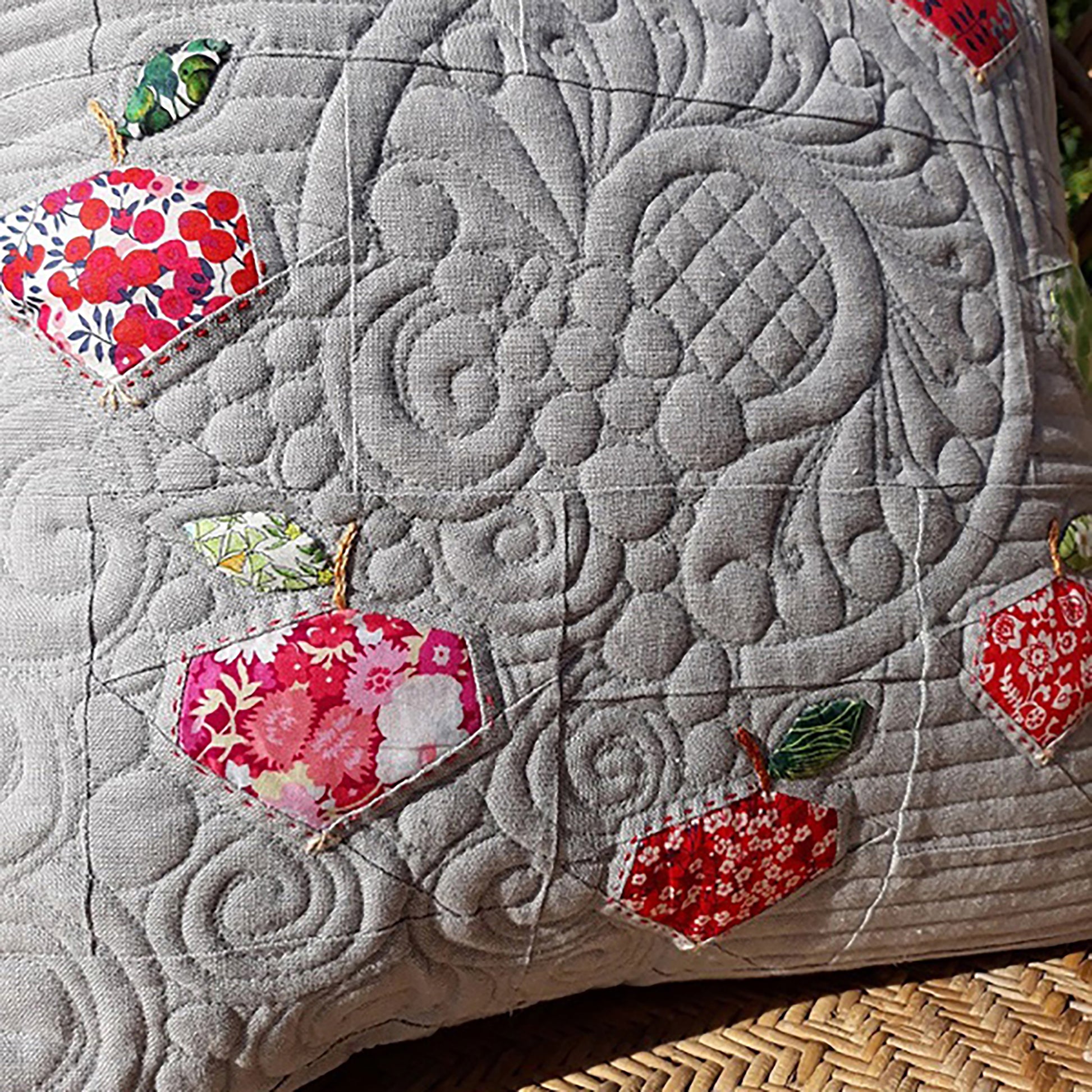 Close up image of beautifully quilted grey pillow with apples. You can see the apples with stems and leaves along with the beautiful quilt work.