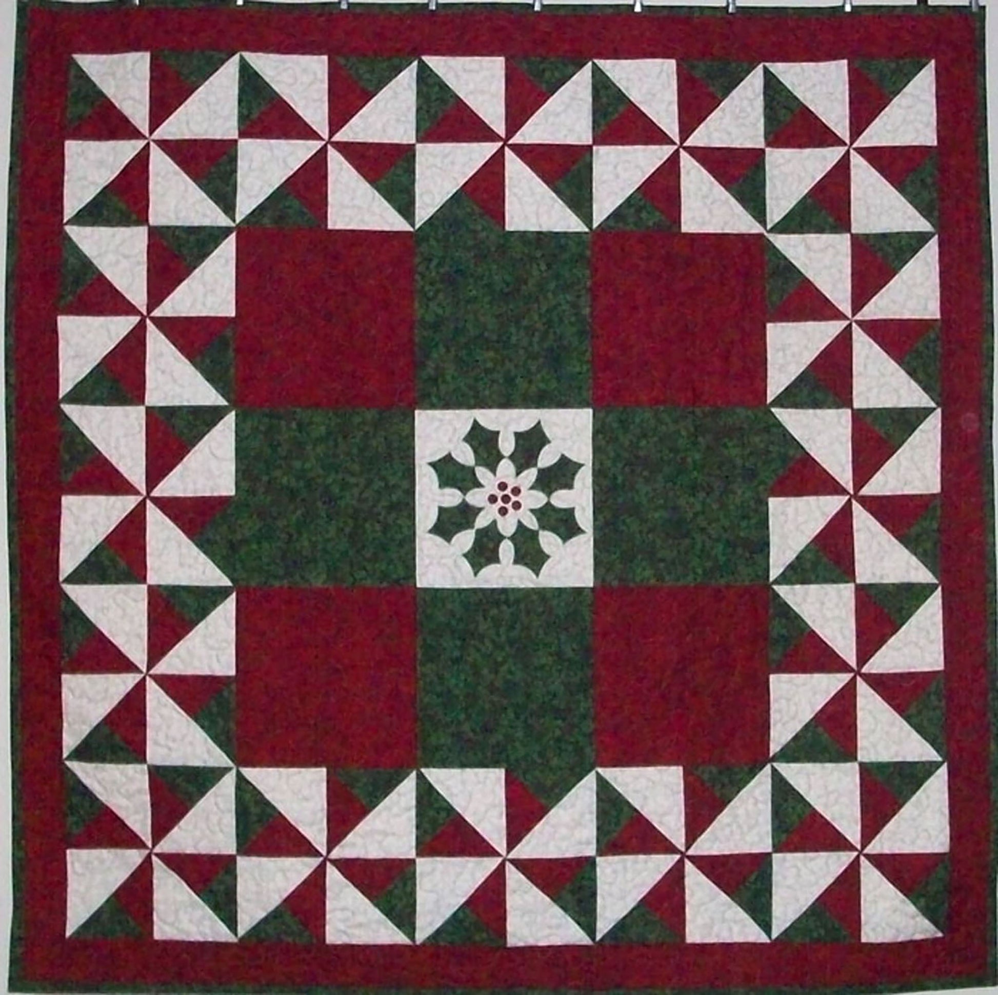 Festive quilt in only red, green and white fabric. The center features a poinsettia design with the border in pinwheel blocks.