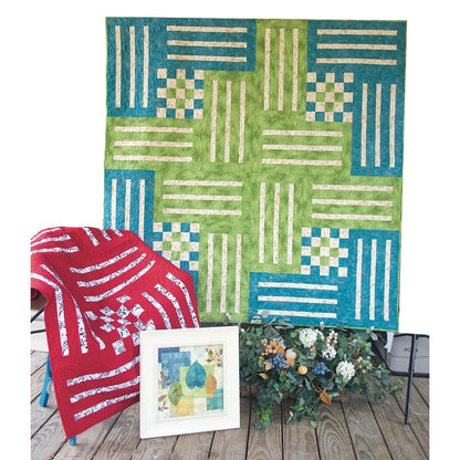 Two pretty quilts featured in this image. Three colored quilt along the wall features blue, green, and cream fabric.  On the bottom on a chair is a two colored quilt in red and a patterned fabric with white.
