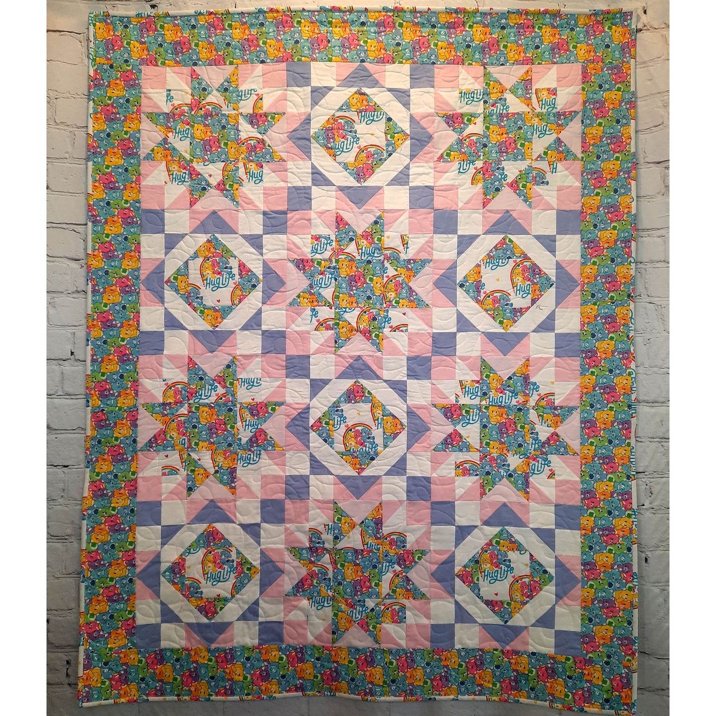 Hug Life quilt features two blocks one star and one diamonds inside each other. This version has bright bear fabric and complimenting pink, purple, and white solid fabric.
