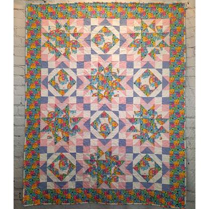 Hug Life quilt features two blocks one star and one diamonds inside each other. This version has bright bear fabric and complimenting pink, purple, and white solid fabric.