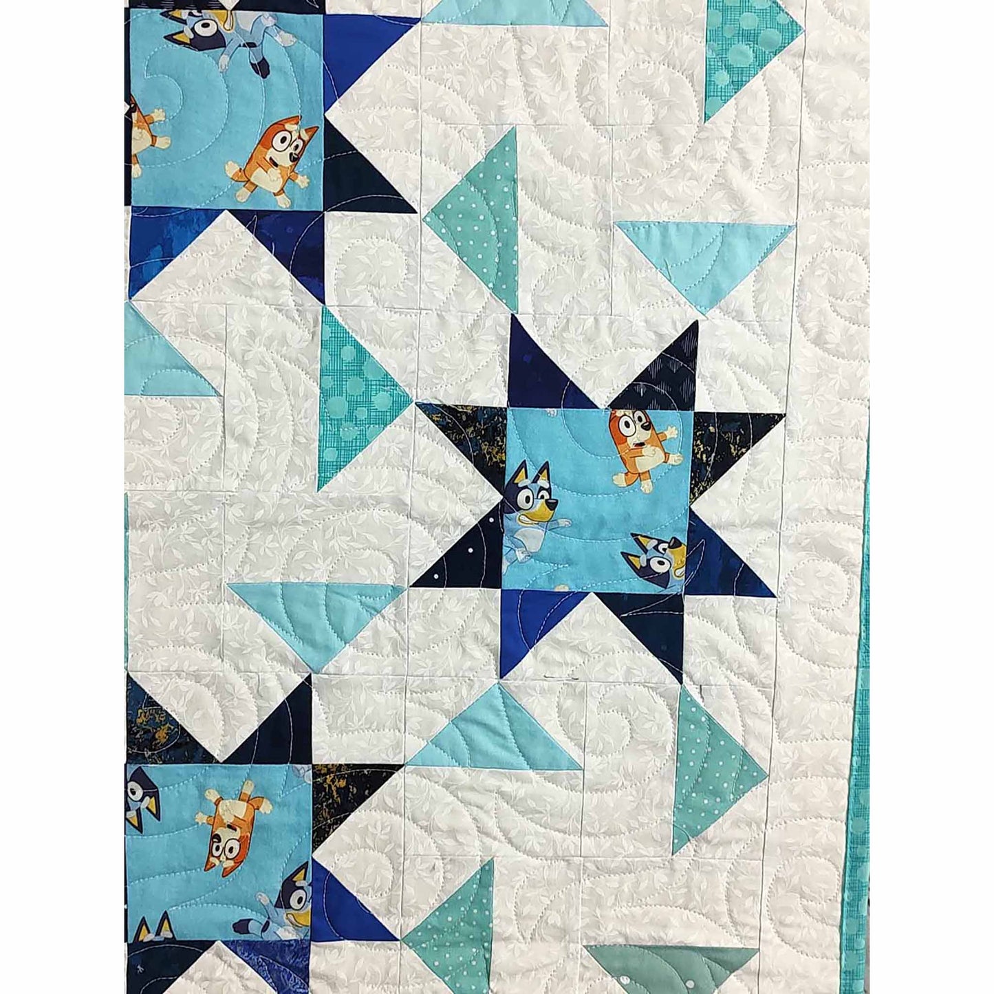 Zoomed into blue and white quilt featuring a star pattern. This one includes Bluey print in the middle of the stars. Close-up so you can see the quilted stitches.