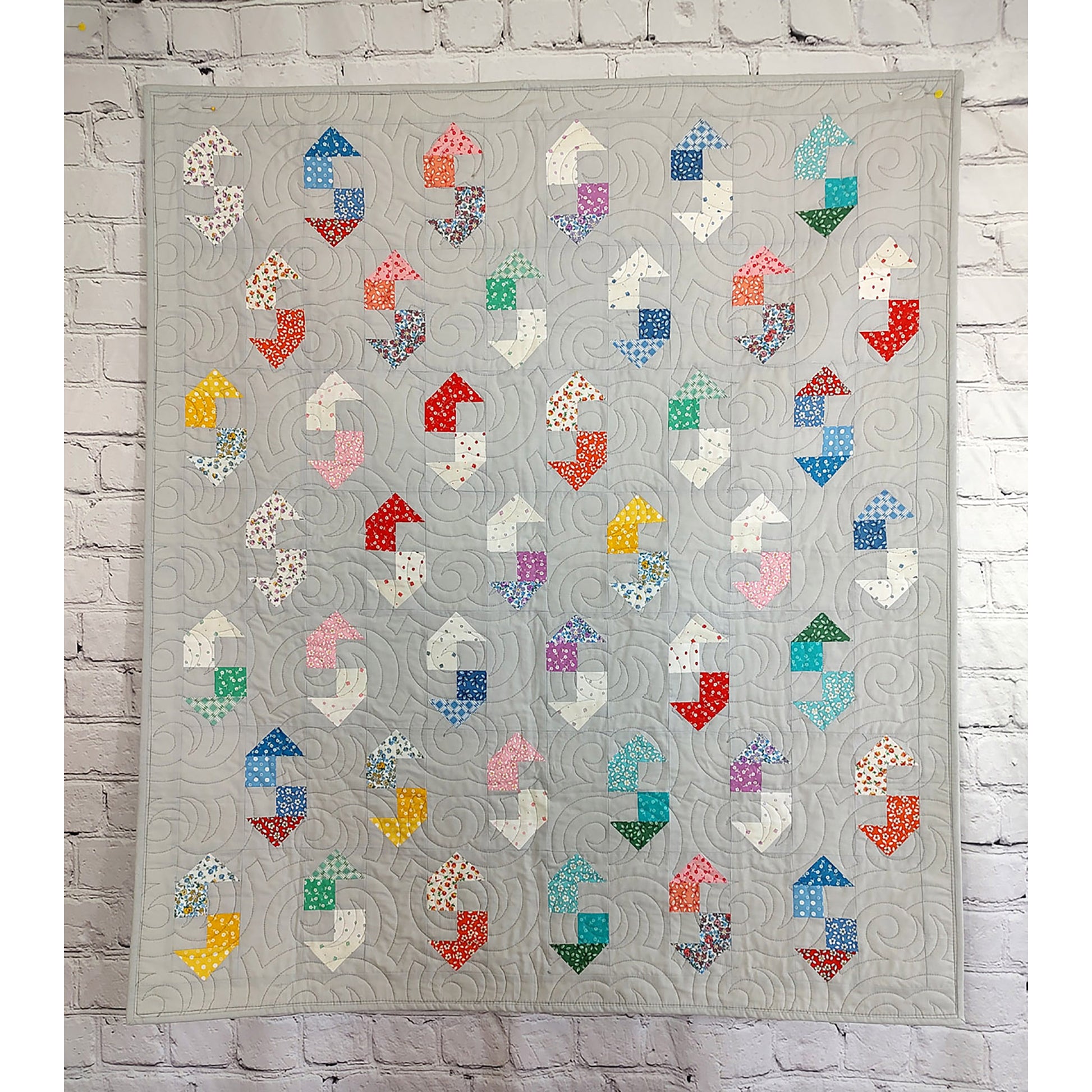 A vibrant quilt featuring an array of colorful shapes, which could look like a wrench, on a gray background.