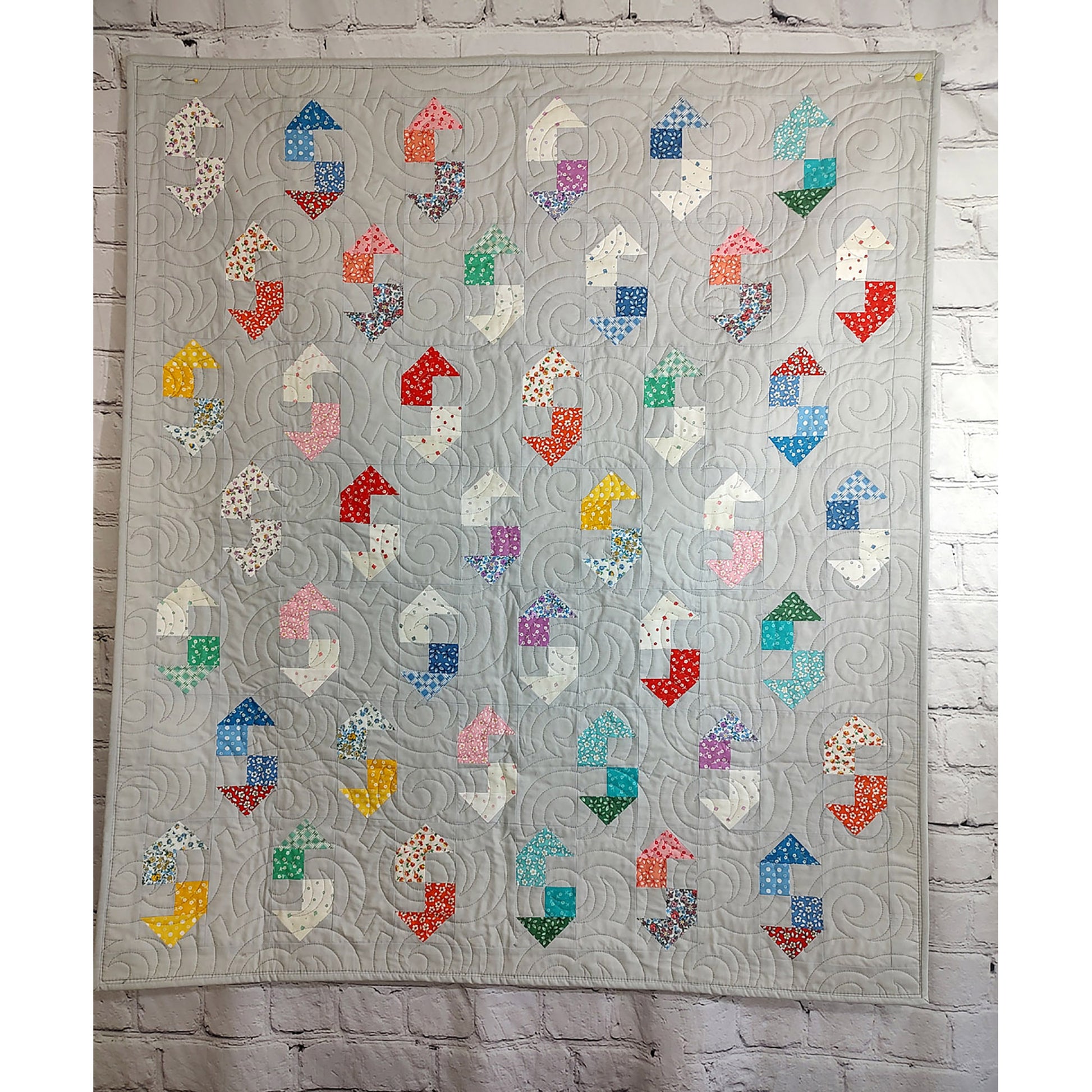 A vibrant quilt featuring an array of colorful shapes, which could look like a wrench, on a gray background.