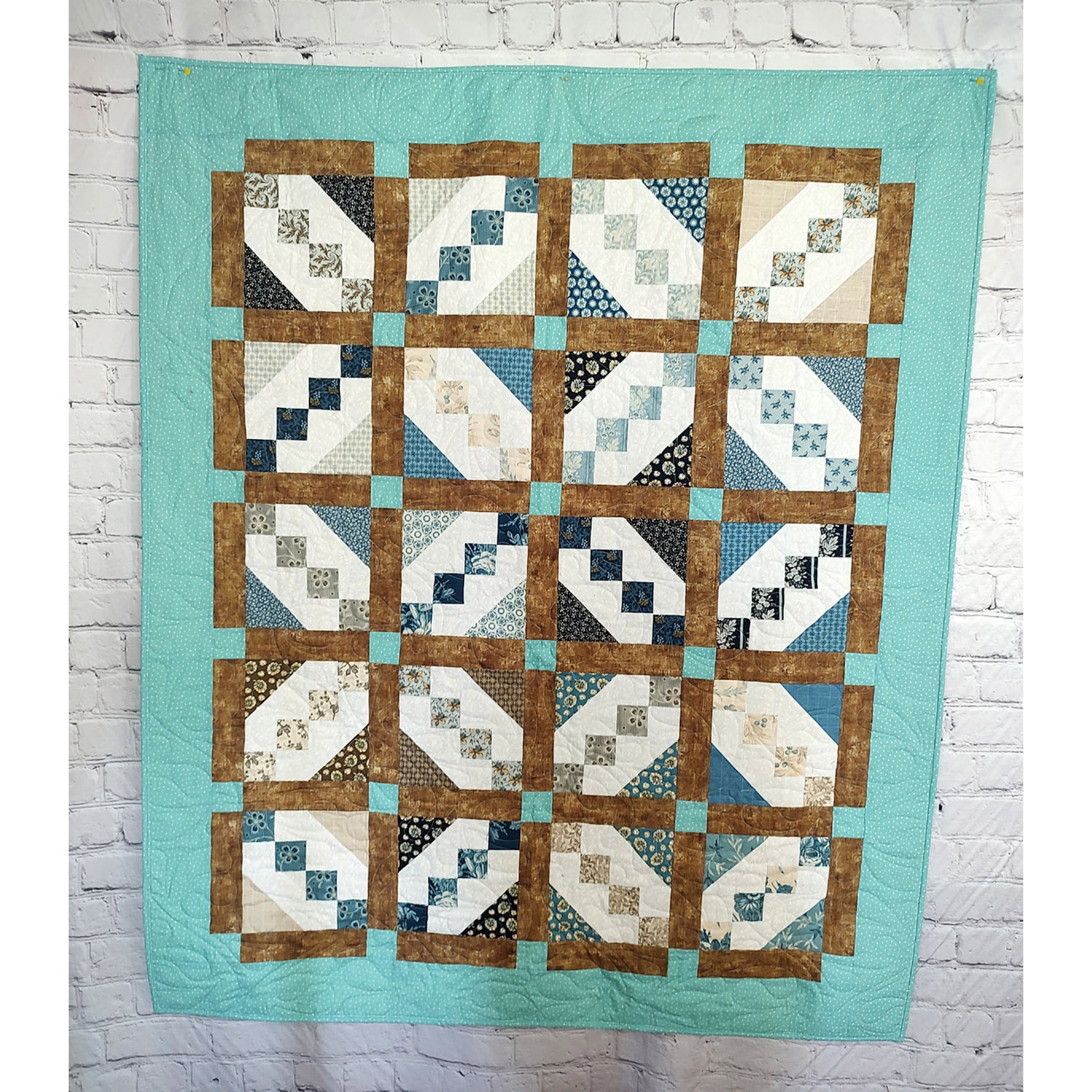 A blue and brown quilt featuring a pattern of squares with smaller blocks at an angle in each square. The finished look gives the feel of diamonds or Xs when you pull out from each individual block with brown fabric between each block.