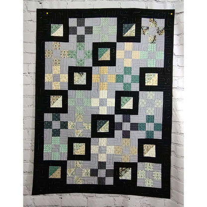 A colorful quilt featuring a pattern of squares and triangles in various hues featuring diagonal rows where the squares have been bordered by a thick black fabric to make everything pop!