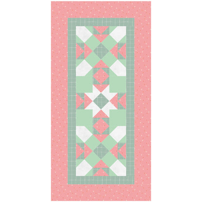 A colorful quilt runner in red and green, adorned with a continuing star pattern down the middle. With the colors, it looks like a Christmas Table Runner.