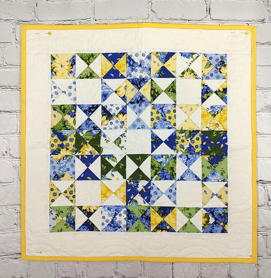 A quilt featuring a vibrant pattern of hour glass blocks in rows and columns in fabric of yellow and blue flowers.