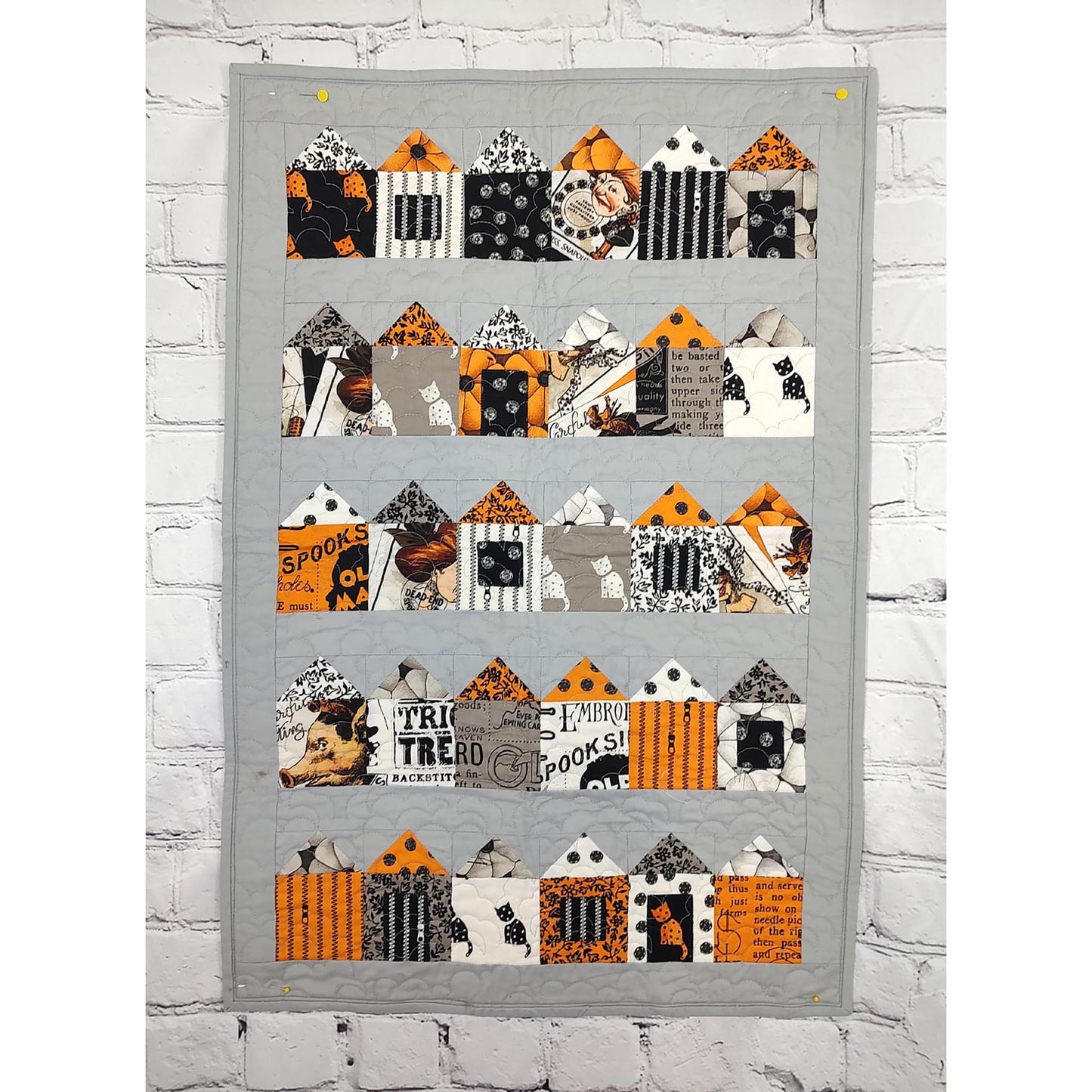 A orange, black, and gray quilt featuring charming house designs in Halloween fabric.