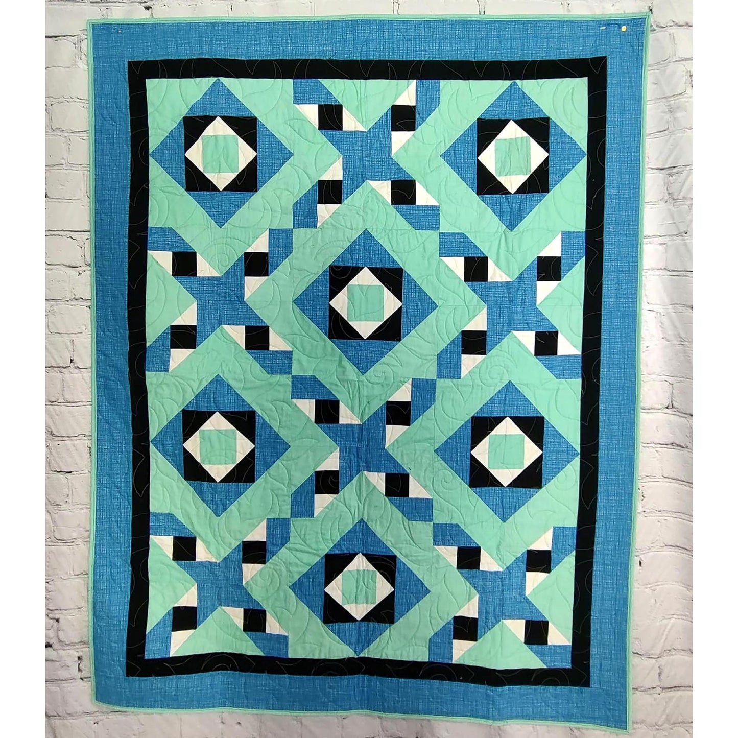 Fun quilt in blue, green, and a pop of black and white features squares inside each other with friendship stars with zig-zag feel between diamonds that were blocks inside each other.