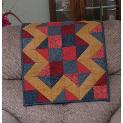 Beautiful quilt draped over a couch features blocks of color with a zig-zag pattern in contrasting pattern on the outside.