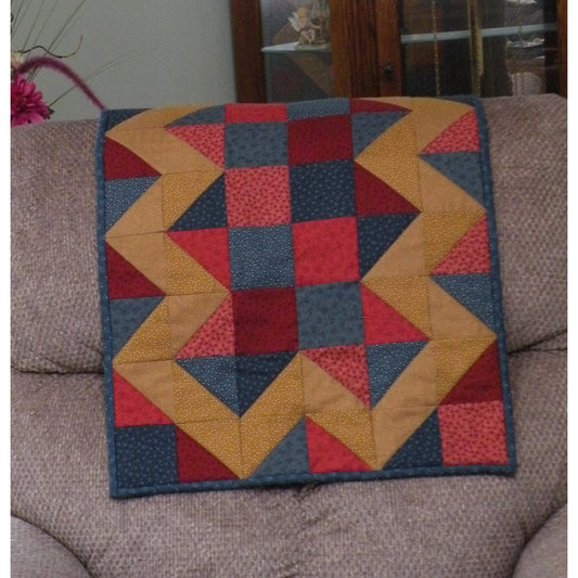 Beautiful quilt draped over a couch features blocks of color with a zig-zag pattern in contrasting pattern on the outside.