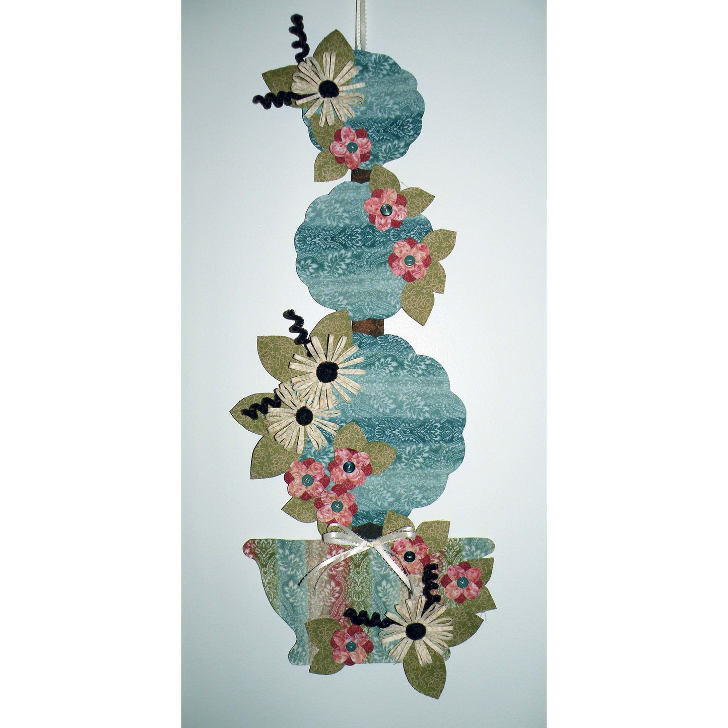 Adorable summer wall hanging features flowers on three levels of topiary in blue-free fabric and pot.