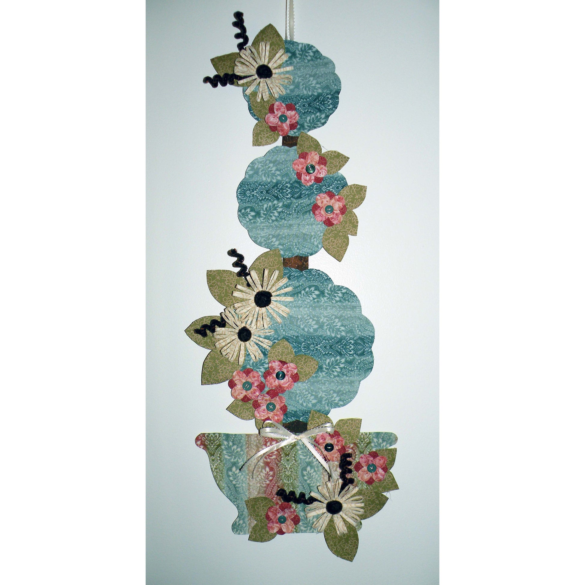 Adorable summer wall hanging features flowers on three levels of topiary in blue-free fabric and pot.