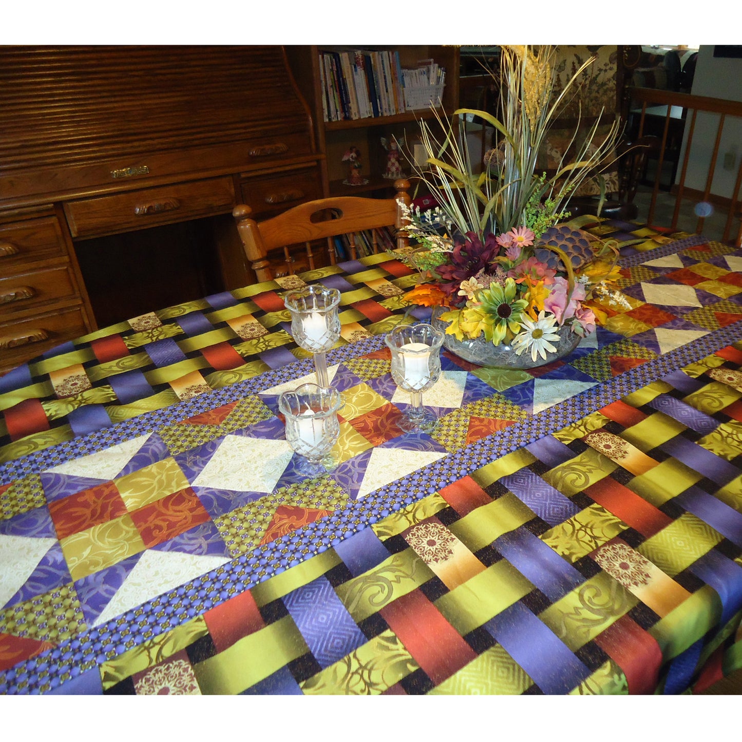 Table set with a beautiful tablecloth featuring a fun table runner like design in the middle. Table has candles and flowers on it.