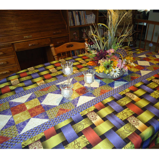 Table set with a beautiful tablecloth featuring a fun table runner like design in the middle. Table has candles and flowers on it.