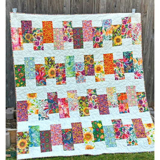 Bright and colorful quilt showcases blocks of different fabrics that are staggered in rows. Many of the fabrics appear to be of flowers and bright colors. The background is white.