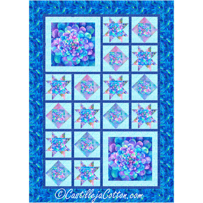 Vibrant blue and purple quilt features two large flowers on the bottom right and top left. The rest of the quilt has smaller blocks broken up with dark blue to form blocks which house either a diamond or an ohio star inside with the same blue and purple colors of the larger flowers. The background color is light blue and there is final dark blue and green border.