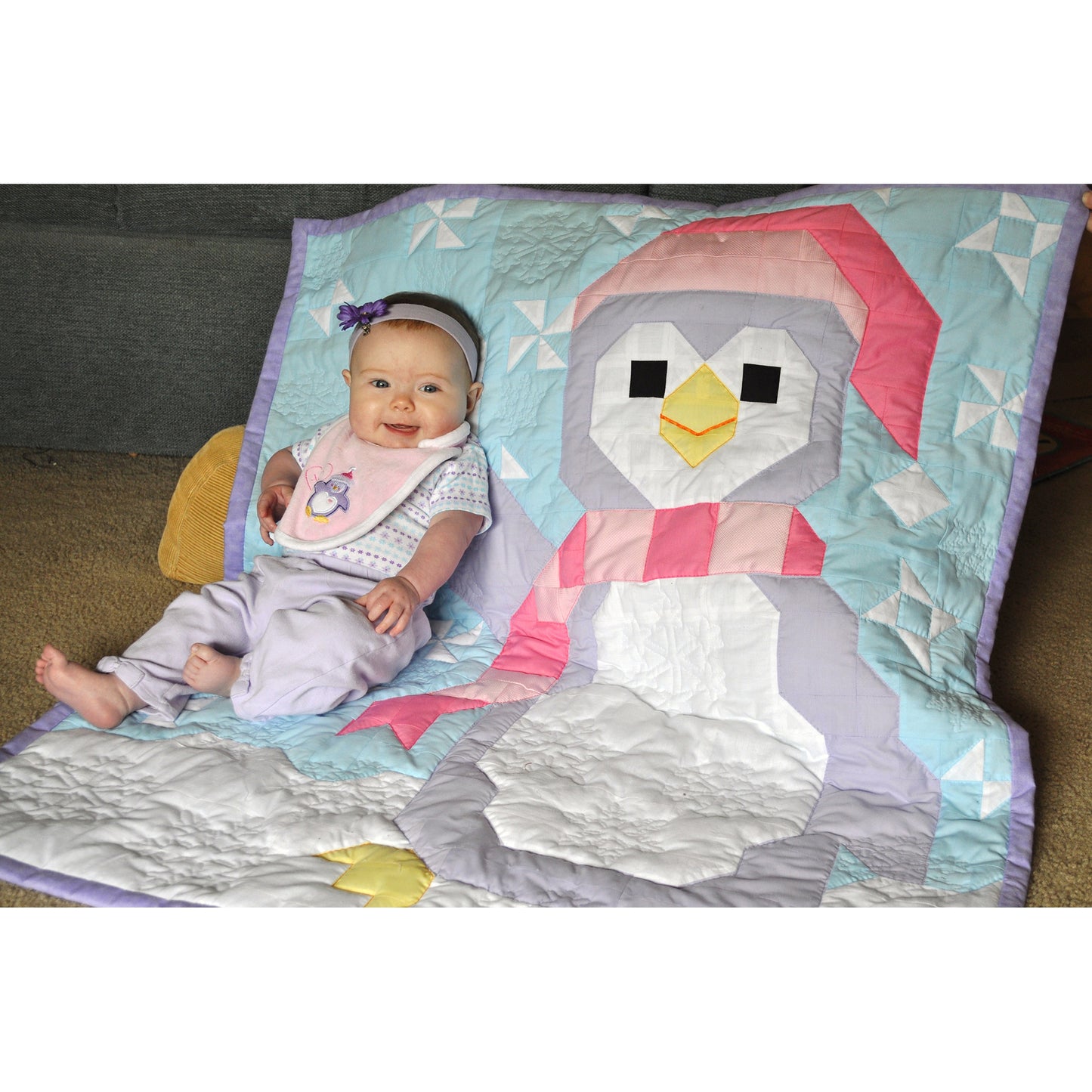 Penguin quilt and a baby the quilt features a large penguin with snow and wearing a hat and scarf.