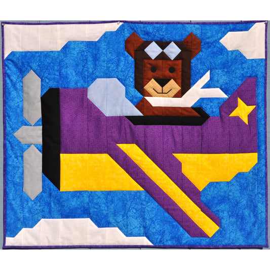 Adorable quilt features a bear flying an airplane in a blue and slightly cloudy sky.