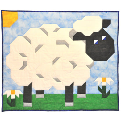 Adorable lamb quilt in the sun with a couple of daisies on the grass.