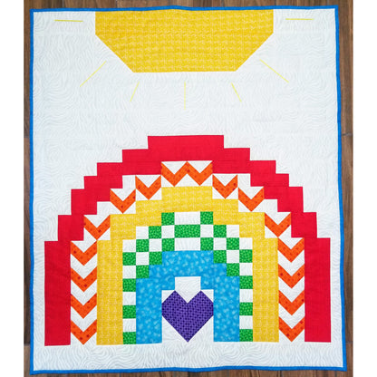 Rainbow quilt features a sun on the top with a pretty rainbow below. Each rainbow color has a different pattern from solid to V or blocks. The middle violet is in the shape of a heart.