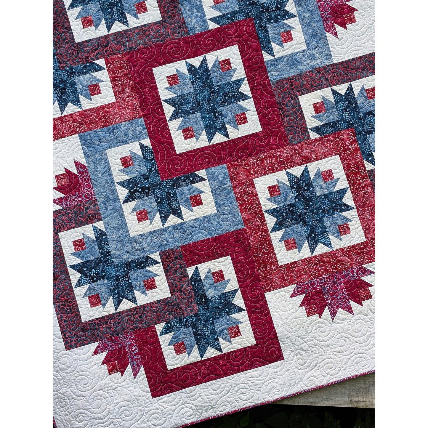 Close up of the beautiful and fun quilt features overlapping star blocks with bold and wide borders to help with the overlapping look. A few additional stars peek out here and there outside those blocks to give a peek-a-boo effect.