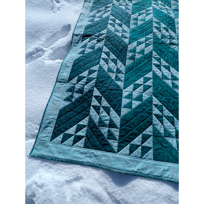 Close up of quilt featuring rows of solid slanted rectangles and ones filled with triangles.  The left rows are darker than the ones on the right.