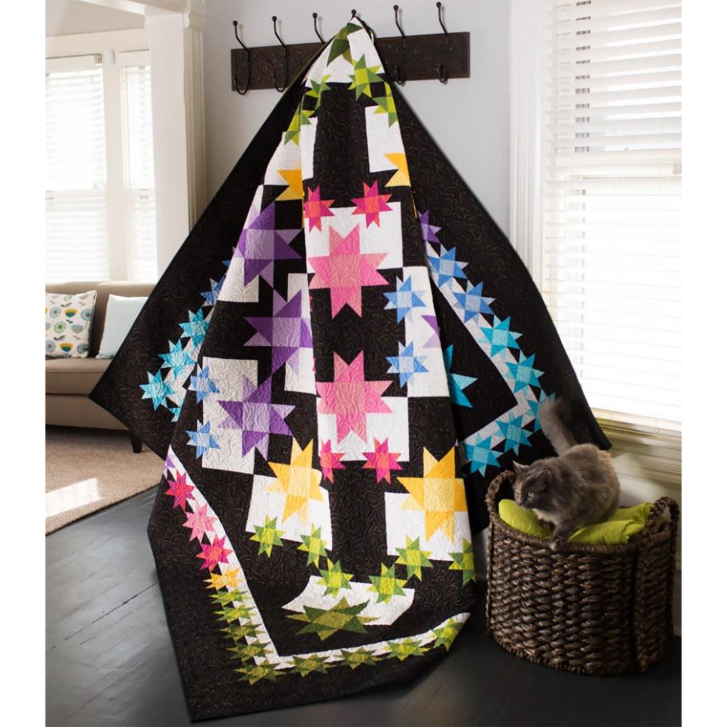 Colorful quilt with star patterns draped over a chair in a room with a cat on a cushion.