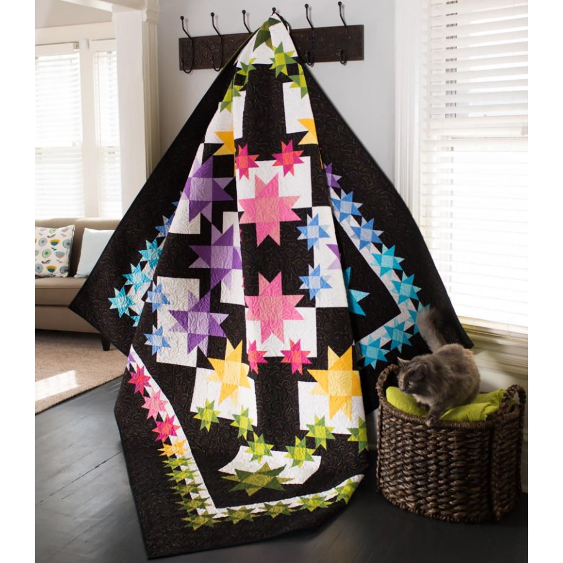 Colorful quilt with star patterns draped over a chair in a room with a cat on a cushion.