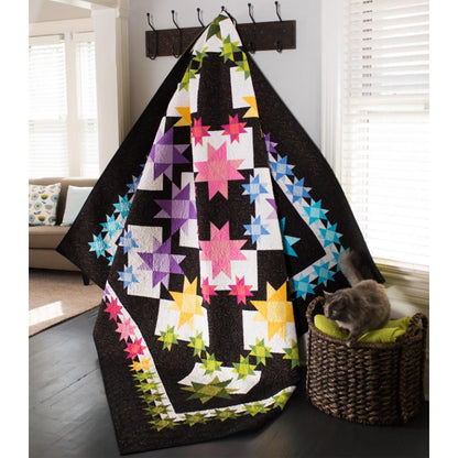 Colorful quilt with star patterns draped over a chair in a room with a cat on a cushion.