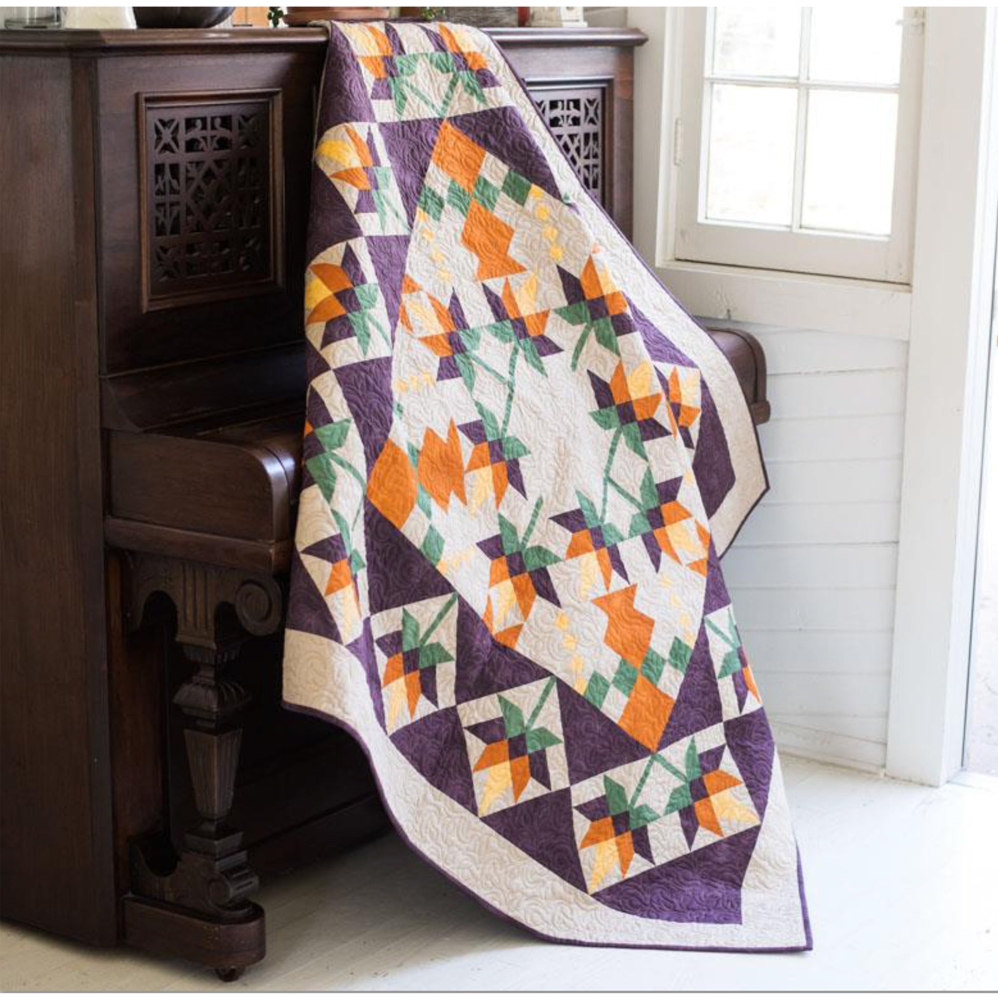 Beautiful quilt features orange flowers in the middle, with a fun pattern for the leaves and in squares around the outside.  Fun for any season.  Shown draped over a piano.