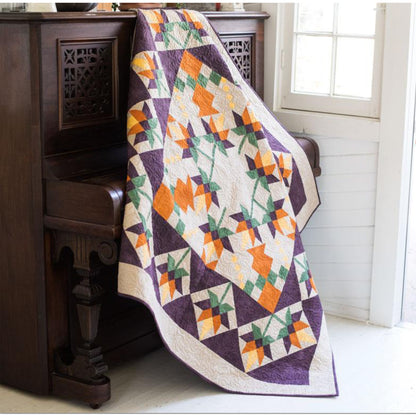 Beautiful quilt features orange flowers in the middle, with a fun pattern for the leaves and in squares around the outside.  Fun for any season.  Shown draped over a piano.
