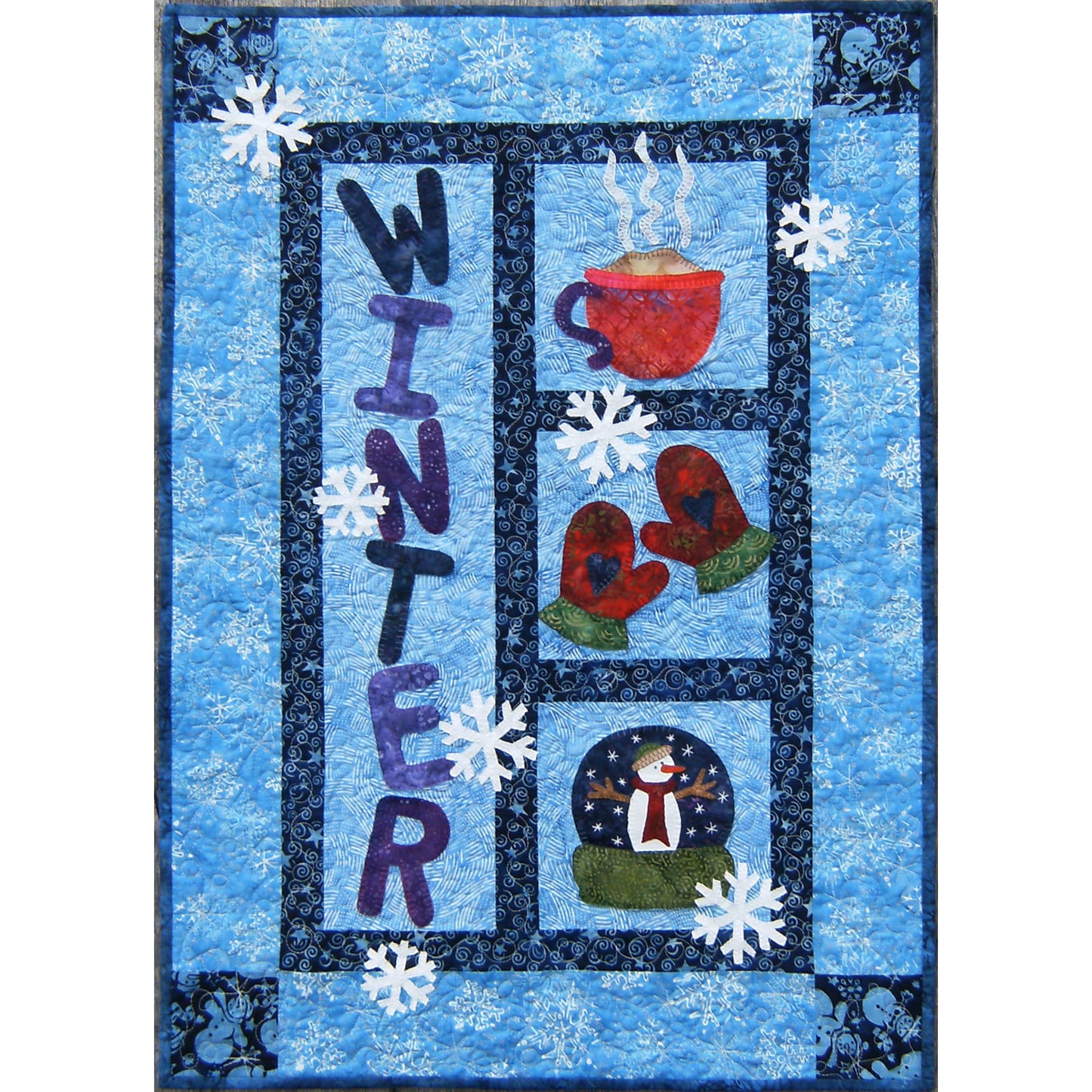 Quilt with winter-themed design featuring a cup, mittens, snowman, and text on a blue background.