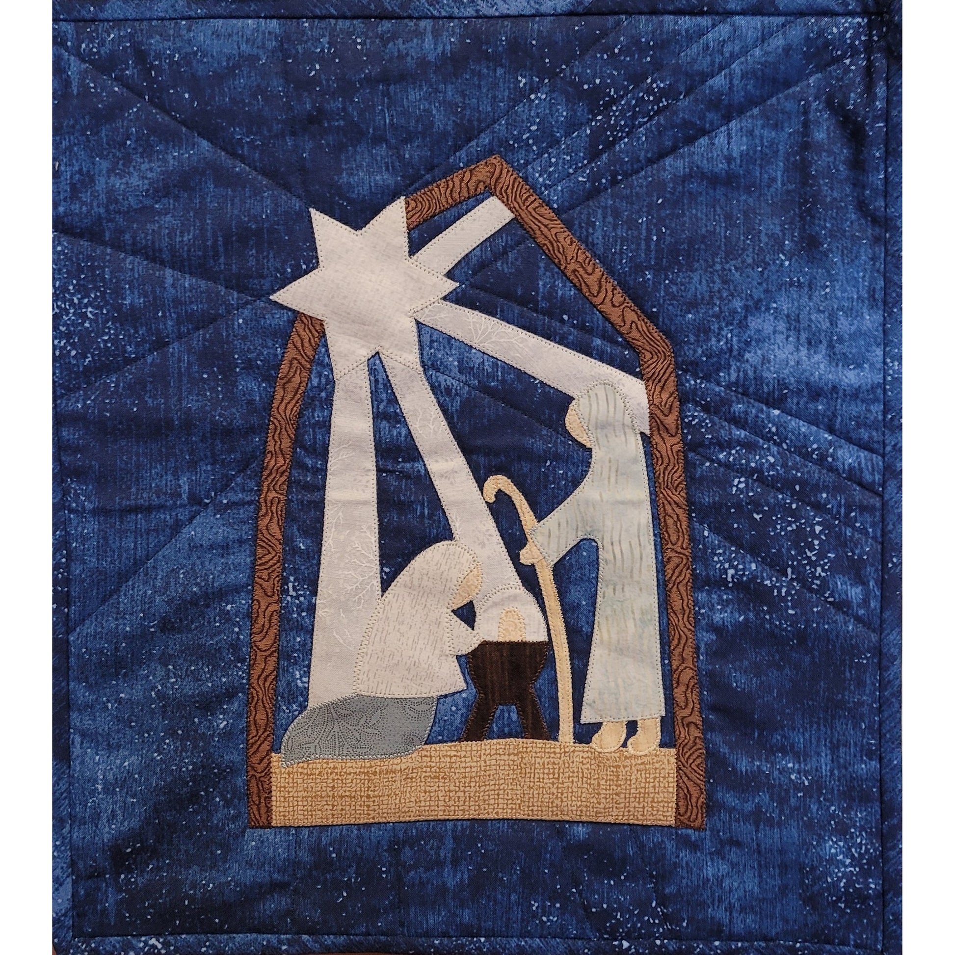 Festive quilt with nativity scene with arch holding up the star to the top left, which is shining down with its beams on the scene below. Below is kneeling Mary, baby Jesus in manger, and standing shepherd with staff. Entire design on blue background fabric.