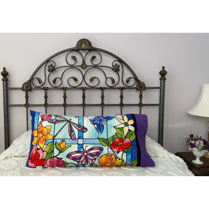 Pillow on a bed with pillowcase showcasing a beautiful butterflies, dragon flies and flowers in front of a stained glass window fabric.