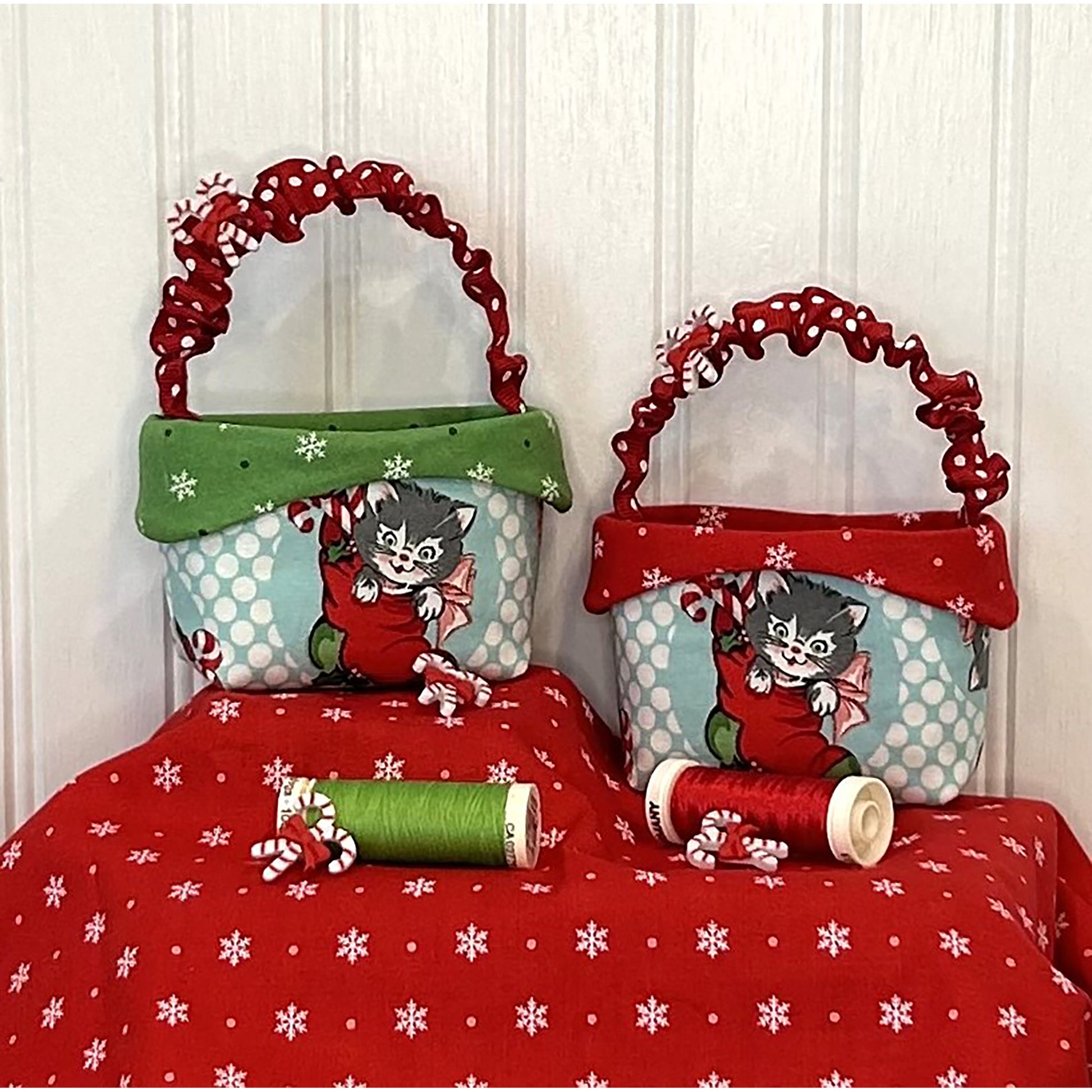 Two adorable baskets showcase cats in stockings fabric with matching handles with candy cane buttons on handle. Size shown with the thread in front with additional candy cane buttons.