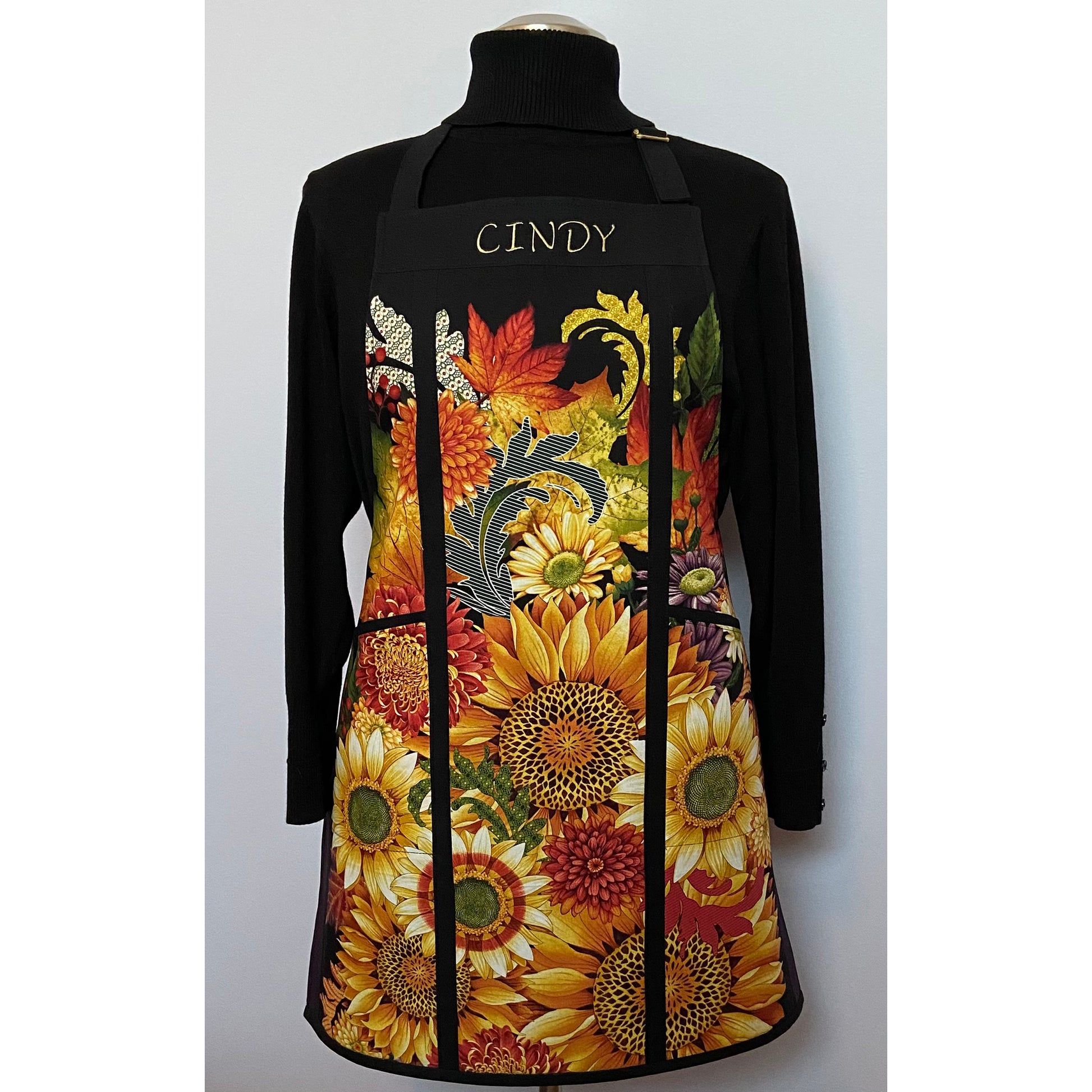 Beautiful apron made of a panel with sunflowers. It is split on the sides with cording and has two large pockets on either side and the name of the owner on the top. 